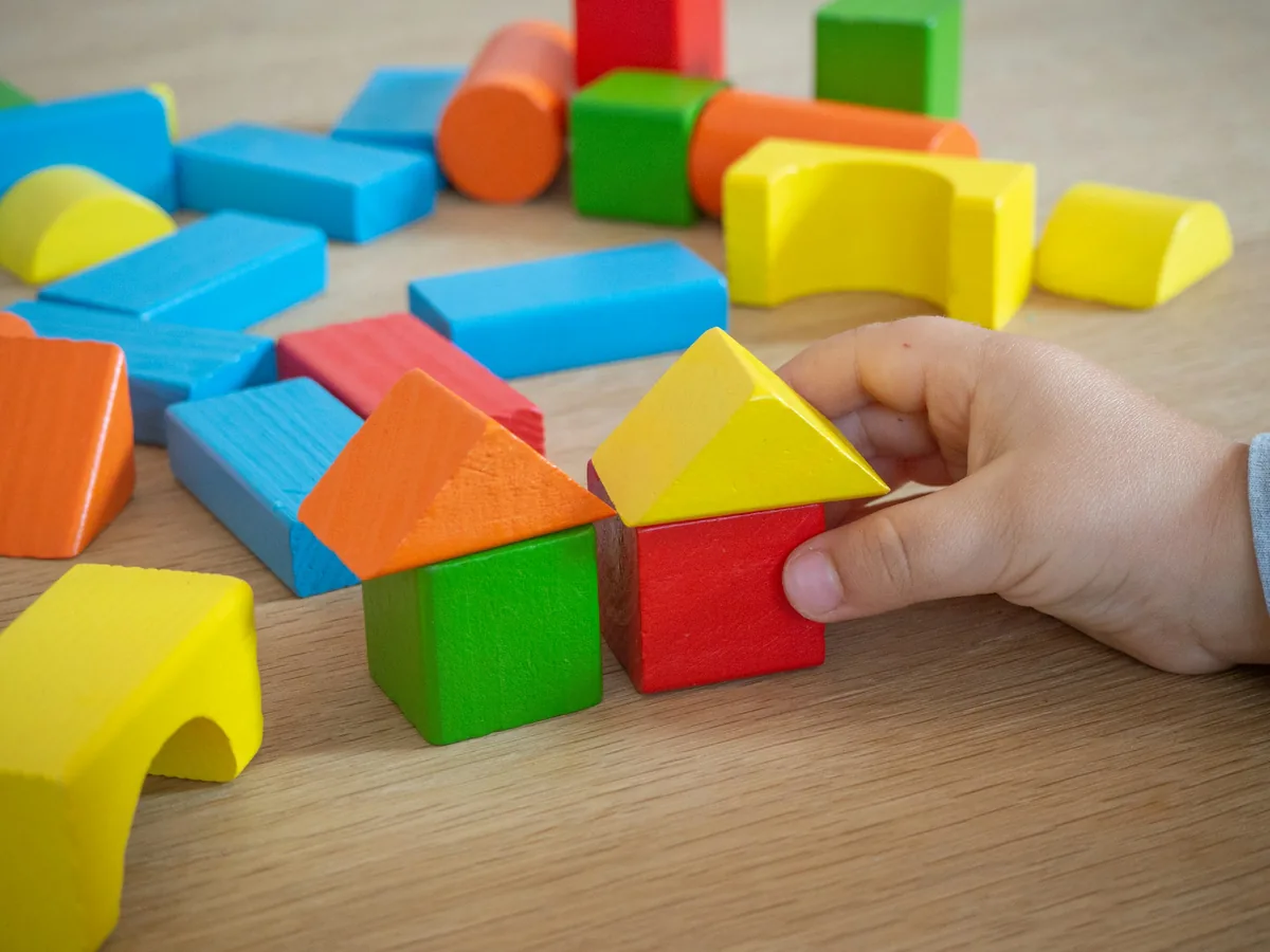 Masa üzerinde renkli ahşap bloklarla iki küçük ev oluşturan bir el